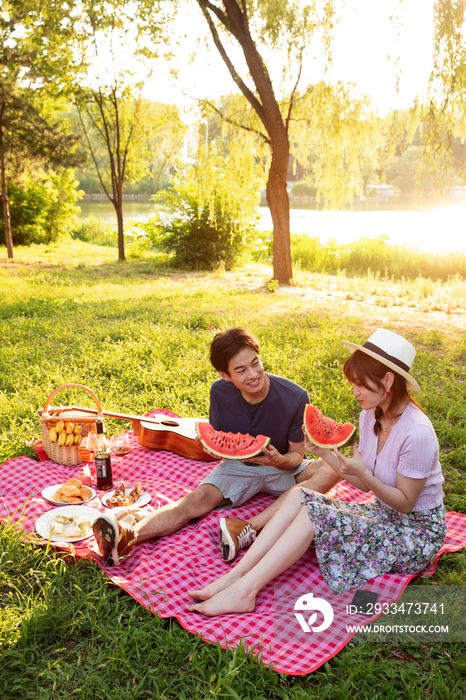 青年情侣坐在公园里吃西瓜