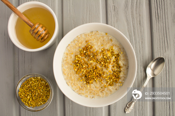 Breakfast: oatmeal with bee pollen and honey  in the white bowl on the grey wooden background.Top view.