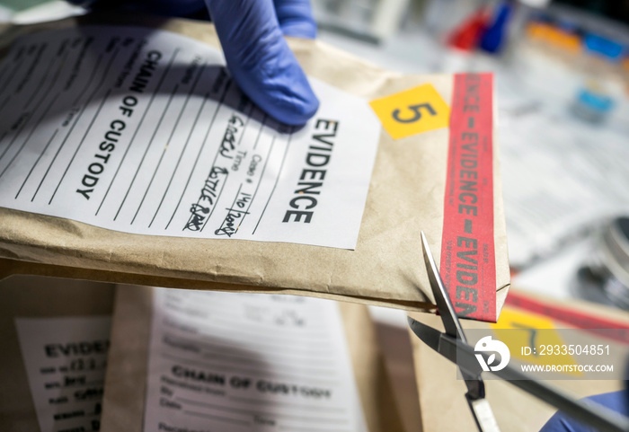 Scientific police opens with scissors a bag of evidence of a crime in scientific laboratory