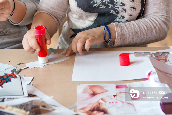 Creative workshop for kids. Little girls gluing cut out shapes and characters from magazines on white paper. Concept of art, crafts, kids having fun. Making collages and creating stories. Messy desk