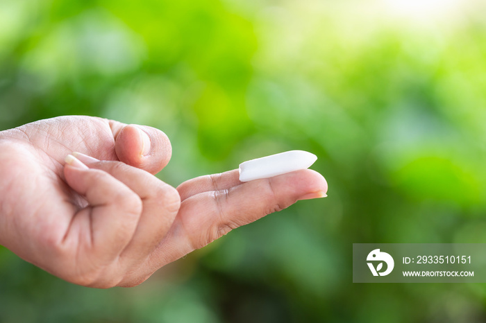 Hand holding suppository candle on green nature light blur background