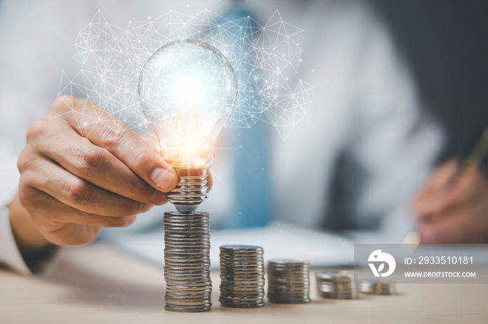 businessman hand holding light bulb with coins stacking on the desk. saving energy and money, the idea with innovation and inspiration concept saving energy and money