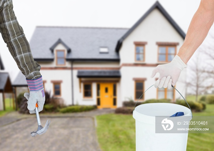 hand with hammer and hand with a cube in front of a real house