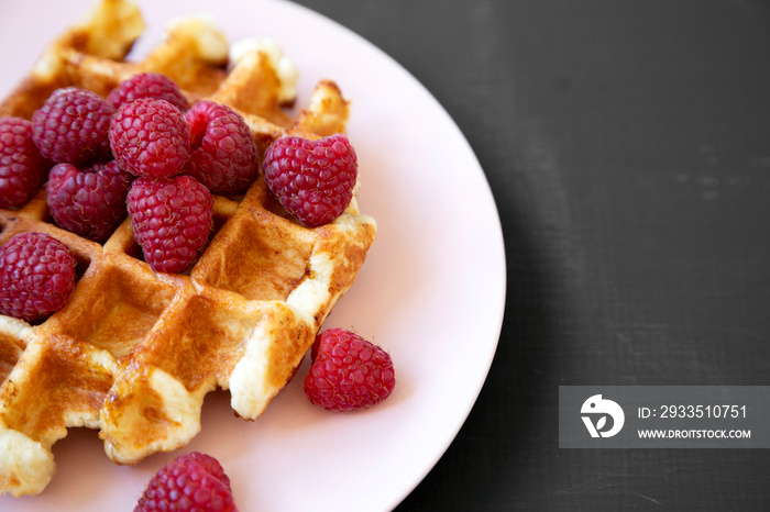 Traditional belgian waffle with raspberries on pink plate over black background, side view. Copy space.