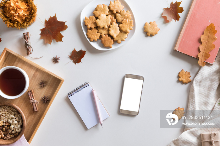 Top view and flat lay of autumn composition background. Notebook, cup of hot tea, book, autumn leaves and flowers, cinnamon cookies on white background.