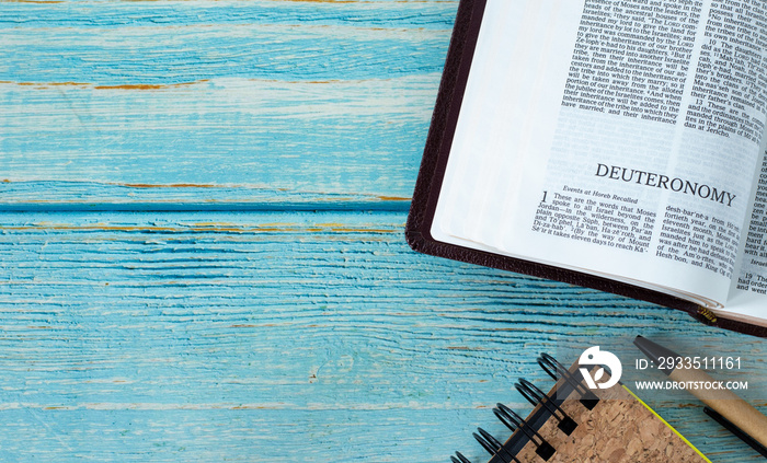 Deuteronomy open Holy Bible Book, notebook, and pen on a rustic wooden background with copy space. Top table view. Flat lay. Studying Old Testament Scriptures. Christian biblical concept. A close-up.