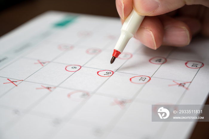 The hand of a man holding a pen in his hand and recording his schedule on a desk calendar.