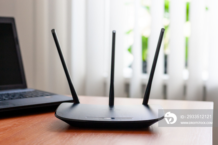 wireless wifi router and laptop at wooden table indoors. window behind. wireless connection concept.