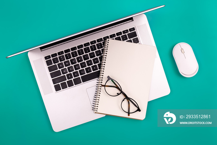 Laptop and blank notepad on a green background, top view, copy space.