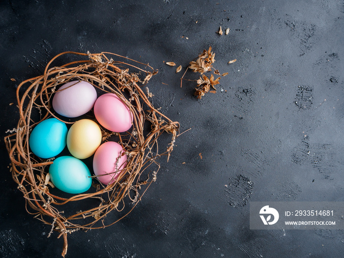 Osternest aus Zeigen mit pastellfarbenen Eiern auf einem schwarzen Hintergrund, Draufsicht, Ostern