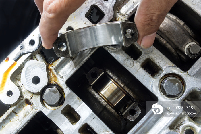 The hand of an auto mechanic picks up the engine connecting rod bearing in check with the engine’s crankshaft on background.