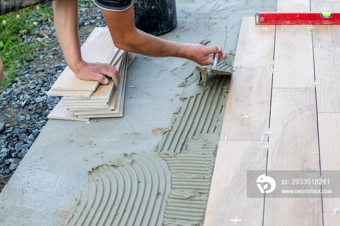 The hands of the professional tiler lying or installing modern, ceramic tile above cement on the garden terrace , tiling floor, building and pavement concept