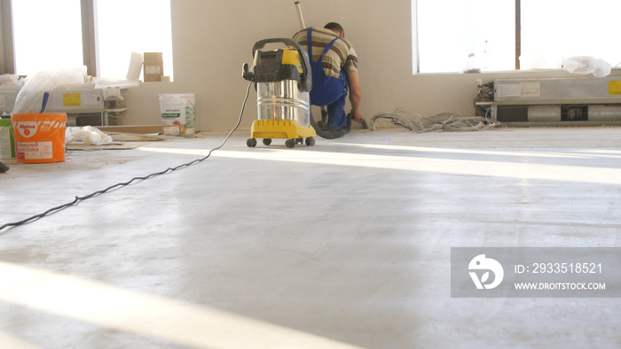 Workers in uniform cleaning room with a vacuum cleaner after installing wood parquet board during flooring work. Man vacuuming floor during repairs