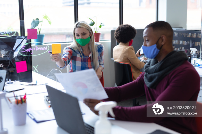 Two diverse business people wearing face masks in creative office