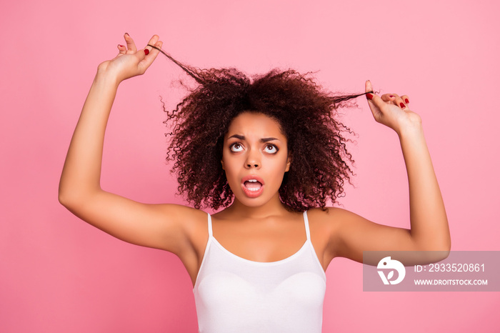 Attractive, pretty, charming girl with wondered, amazed, impressed reaction and wide open mouth, worry about her damaged hair, holding two strands with hands looking up over pink background