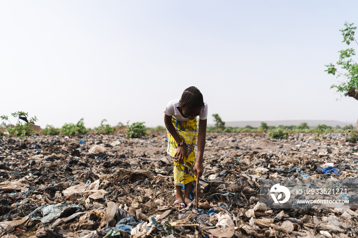 Young African girl digs in a rubbish dump in search of reusable material; informal waste recycling