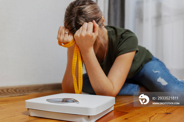 White scale and depression, upset and sad woman with measuring tape on wooden floor