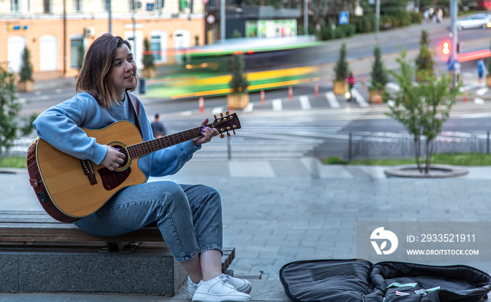 Female musician busking playing acoustic guitar and singing outdoors in street.