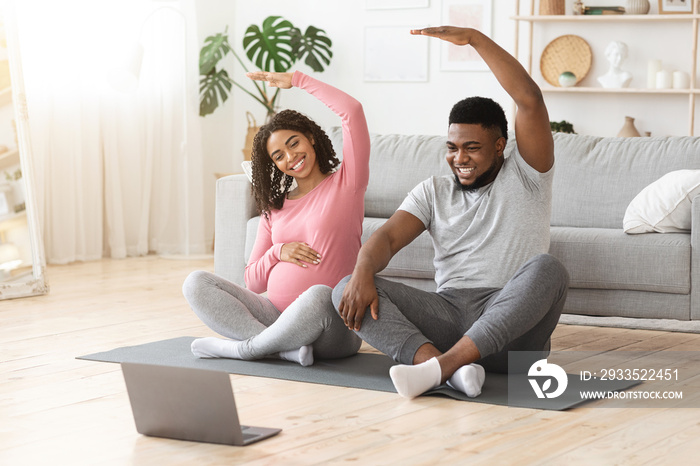 Cheerful black expecting couple exercising together at home