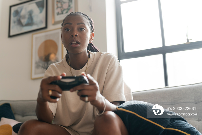 Serious young woman playing video games while sitting on sofa at home