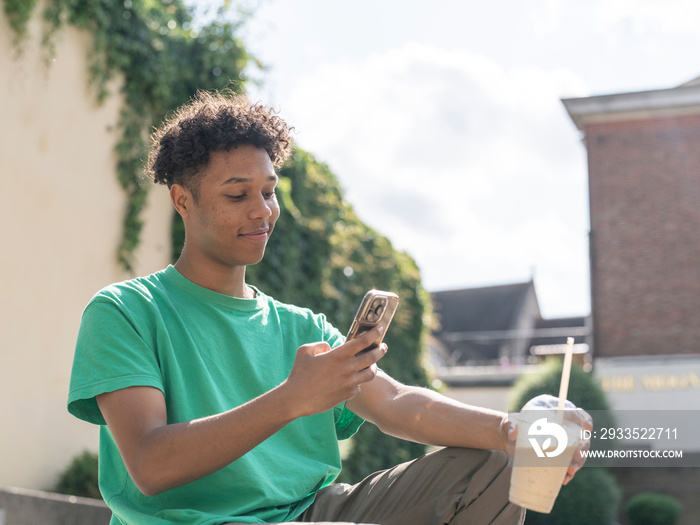 Young man photographing smoothie with smart phone on sunny day