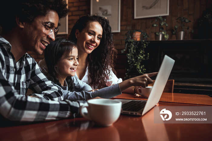 Happy multiethnic family having fun while using laptop together at restaurant