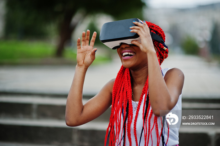 Fashionable african american business woman at pink pants and red dreads with virtual reality glasses outdoor.