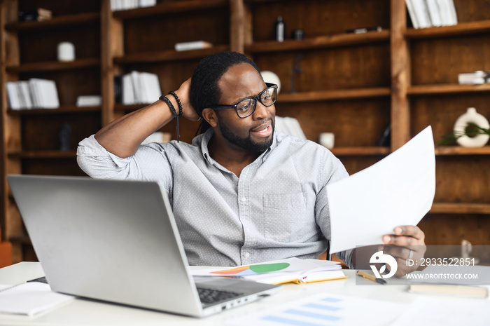 Latin businessman sits at desk in home office near laptop, touches back of the head, thinks over strategy work, generating new fresh ideas, searching solution, trying to figure out the statistics