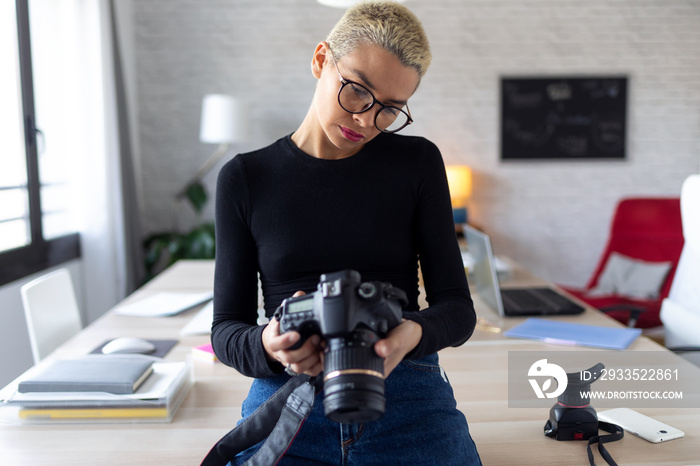 Modern young entrepreneur woman reviewing her last photographs in the camera while sitting in the office.