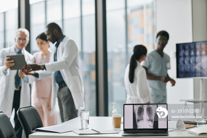 Diverse group of doctors collaborating in conference room with focus on laptop screen in foreground, copy space