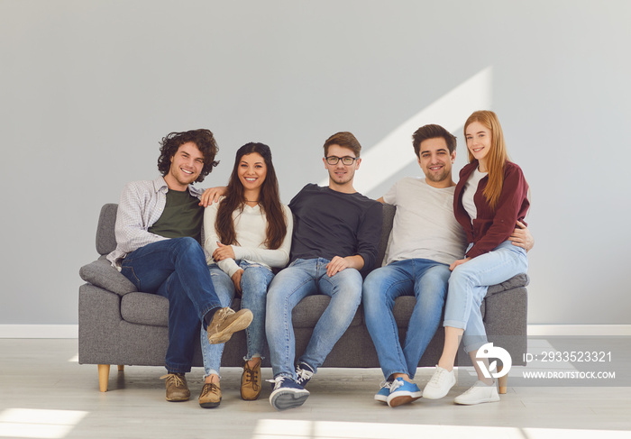 A group of friends is sitting on couch in a room on a gray background.