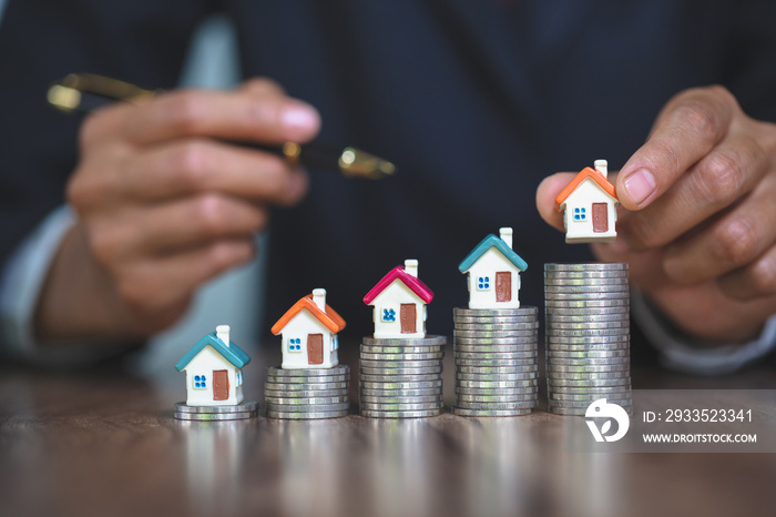 Woman hand hold a  home model put on the stack coin with growing, Savings money for buy house and loan to business investment for real estate concept.