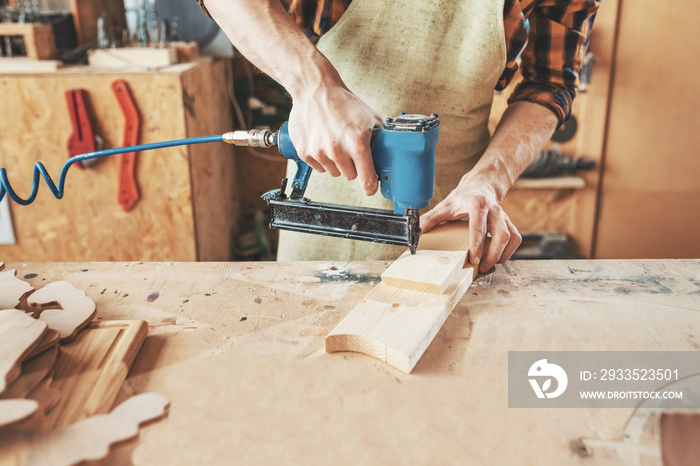 Carpenter using nail gun to crown wooden boards in workshop. Craftsman equipment concept