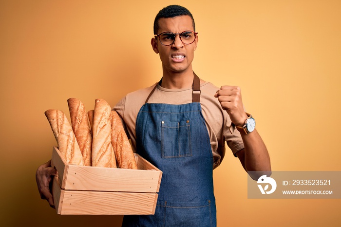 Young handsome african american bakery man holding wooden box with healthy fresh bread annoyed and frustrated shouting with anger, crazy and yelling with raised hand, anger concept