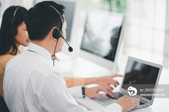 Team of call center staff in Asia wears headphones with a microphone. Smile while serving customers at desks and computers. Service concept and consulting. Communication concept.