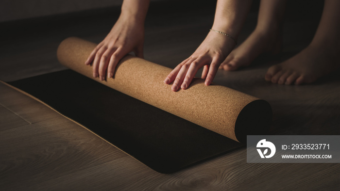 Selective light focus of woman unrolling cork yoga mat to practice yoga. Concept: self care routine practices at gome