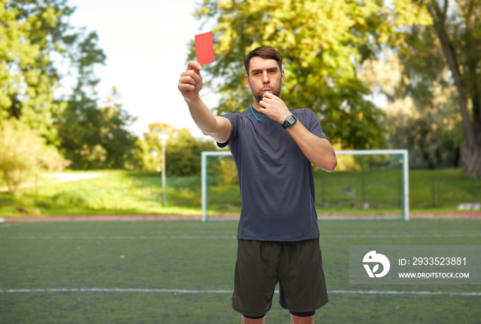 sport, football and refereeing concept - male referee whistling whistle and showing red penalty card over soccer field background