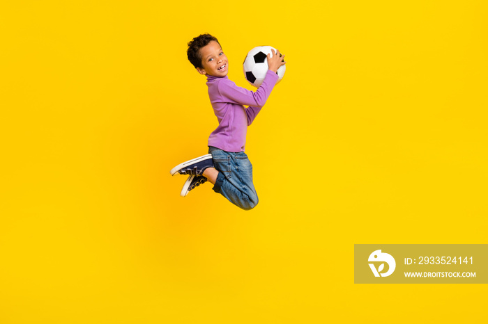 Full length portrait of active sportive person jumping arms hold football isolated on yellow color background