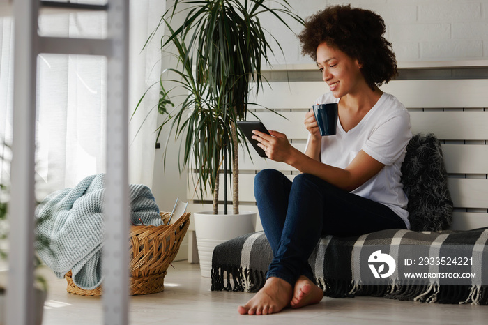 Pretty African American young woman reading an eBook at home at her cozy corner