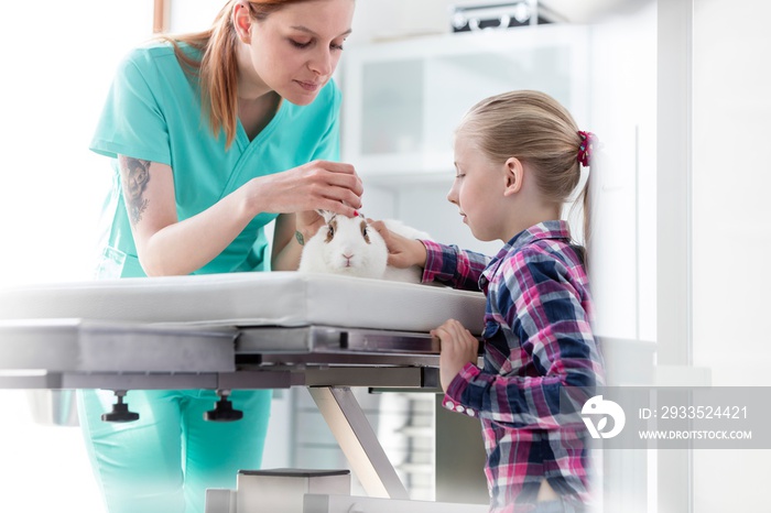 Young attractive vet examining rabbit with child owner in Veterinary clinic