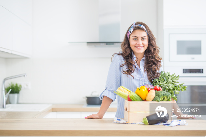 Woman in her kitchen with wooden box full of organic vegetable