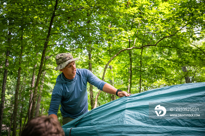 Air Force service member sets up a tent with his sons on  a backpacking trip.