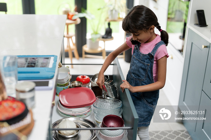 Little girl taking mug from drawer in kitchen