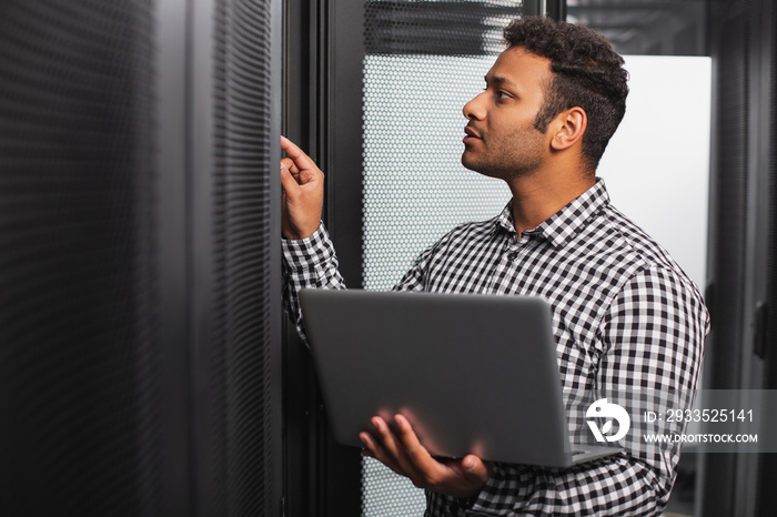 Server room. Focused IT guy using laptop and pointing at hardware