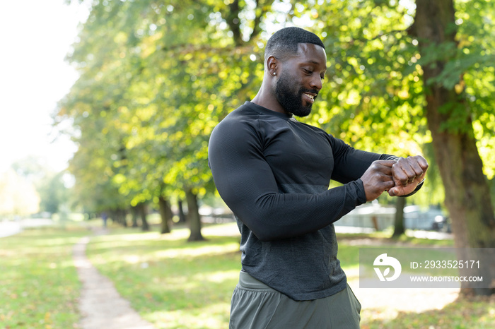 Smiling athletic man checking smart watch in park