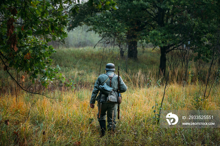 Single Re-enactor Dressed As German Wehrmacht Infantry Soldier In World War II Walking In Patrol Through Autumn Forest. WWII WW2 Times