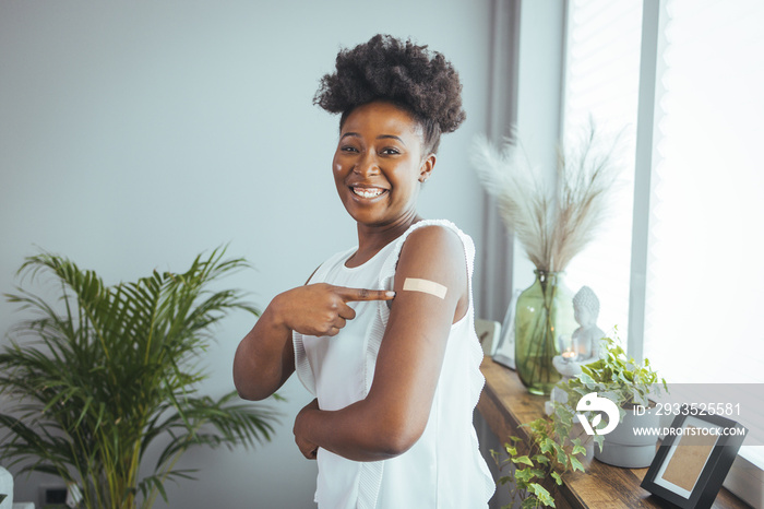 Cheerful vaccinated African-American woman showing arm with medical patch and laughs, black female getting vaccine dose against covid, plaster on her shoulder, isolated on white. Healthcare concept