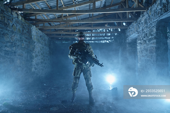 Portrait of airsoft player in professional equipment with machine gun in abandoned ruined building. Soldier with weapons at war