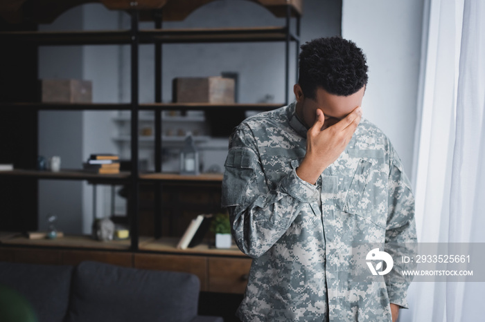 Stressed African American soldier in military uniform suffering from PTSD at home