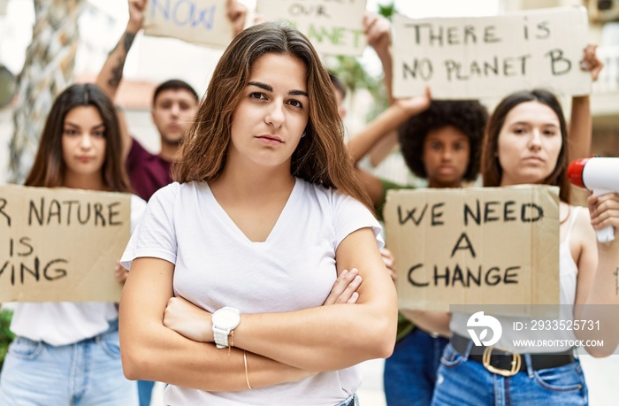 Young activist woman with arms crossed gesture standing with a group of protesters holding protest banner at the city.